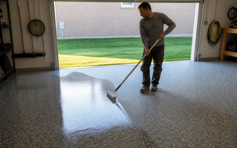 A worker rolling a glossy coating onto a garage floor.